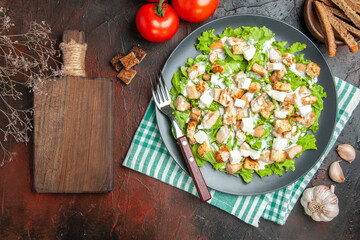 top view caesar salad on oval plate green white checkered napkin chopping board garlic on dark red background