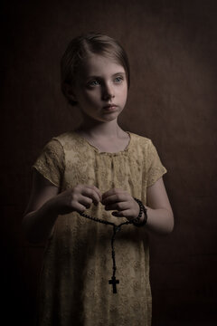 Classic portrait of a young girl praying holding a rosary in her hands