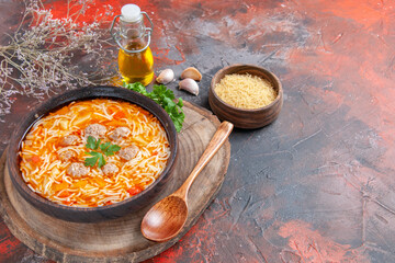 Horizontal view of delicious noodle soup with chicken on wooden cutting board greens spoon oil bottle garlic on dark background