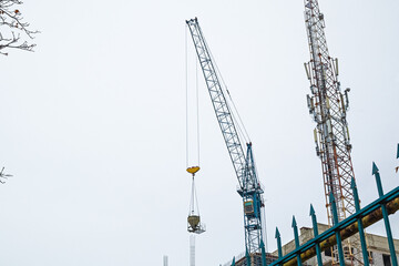 The Hoisting Tower Crane Moves the Concrete Mixer to The Workplace at The Construction Site. A Cell...