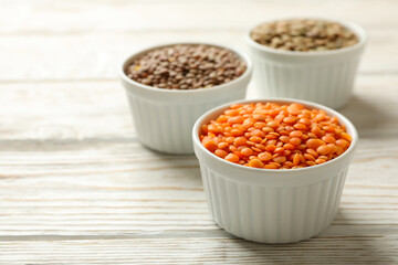 Bowls with different legumes on wooden background, space for text