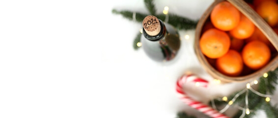 wine cork with the number 2021 in the foreground and blurred tangerine basket, fir branches, garland lights and striped candy on a white table top view. atmosphere of meeting the new year