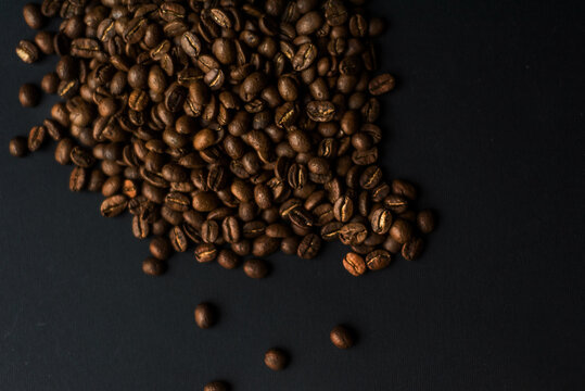 Close up of brown coffee beans in natural light on black table, black background in a dark theme. Moody picture with shadows. Sun rays.