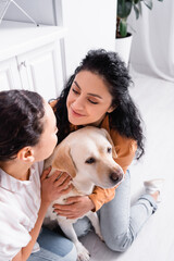 high angle view of happy hispanic lesbian women looking at each other while hugging labrador dog