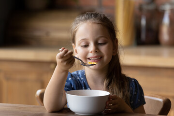 How tasty. Cute little girl enjoy eating cereal for morning breakfast with appetite. Hungry child...