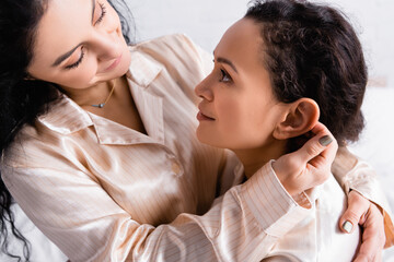 Obraz na płótnie Canvas Hispanic woman touching lesbian partner in pajamas at home