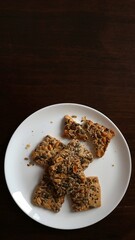 sweet food background in brown tones with white plate visible from above with scattered cookies and blank copy space, homemade baked goods with healthy ingredients and space for text on dark surface