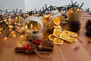 Rustic style christmas diy, handcrafted, handmade ornaments and decorations, cinnamon stick and dried oranges falling from glass jar with lights in the background, top view