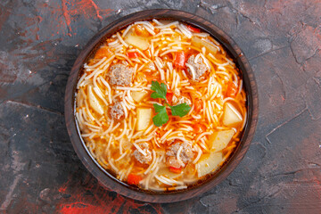 Top view of noodle soup with chicken in a brown bowl on dark background