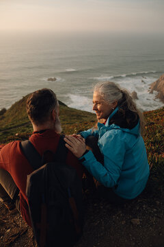Senior couple talking to each other enjoying sunset sitting on cliff at ocean