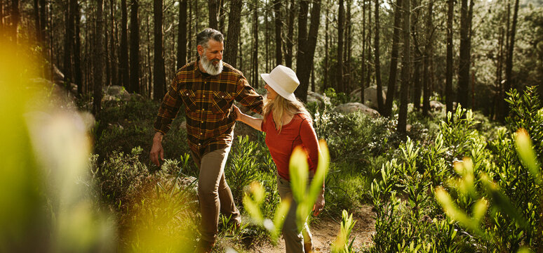 Senior couple hiking through forest on a sunny day together - Powered by Adobe