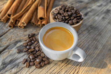 Hot coffee espresso  in a white glass, cinnamon coffee beans on a wooden table.
