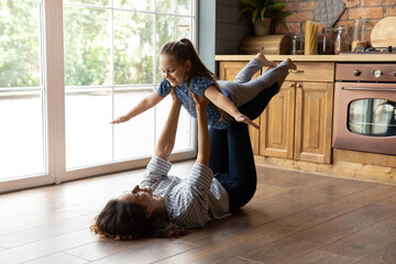 Cute gymnastics. Happy smiling young mom supporting little daughter in air doing flying plane...