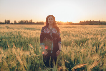portrait of young brunette female looking at camera in wheat field during sunset