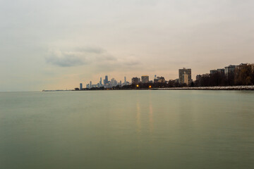 Chicago skyline in the distance with calm lake and sunset light on cloudy evening