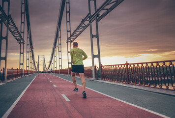 sporty man running outdoors on the bridge during sunrise