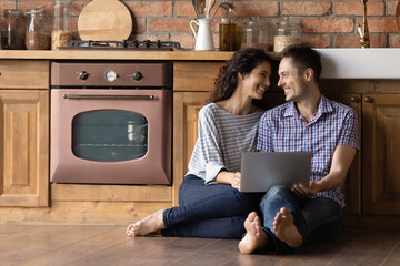 Warm relations. Millennial spouses renters of new house sit on cozy heated floor at modern kitchen...