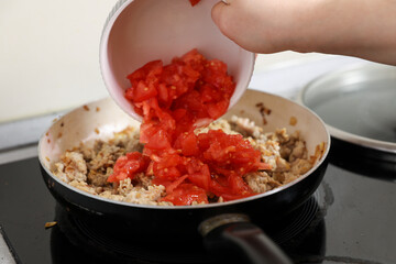 young housewife fry meat in a pan and electric stove. Cooking dinner at home.