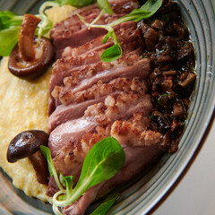 Healthy dish made of grilled duck fillet and corn porridge decorated with mushrooms and greens. Ground mushrooms sauce. Square photo. Closeup.