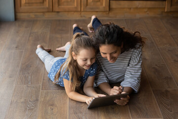 Funny learning. Happy small daughter and positive young mommy lie on warm wooden floor look at...