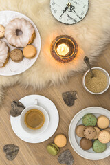 Fototapeta na wymiar Scene of a cozy coffee break with macarons, donuts, biscuits and candle on lambskin and wood