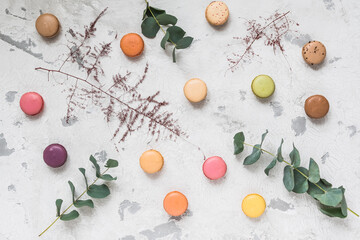 Colorful french macarons on white rustic background, decorated with eucalyptus leaves, top view