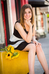 A young Caucasian Armenian girl holding a yellow suitcase and yellow sunflowers in an urban setting