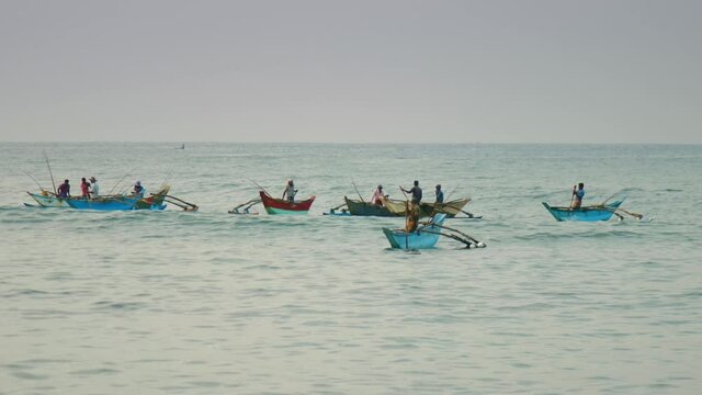 Poor local people on traditional rowing boats catch fish with rods in calm ocean against clear sky. Concept marine fishing