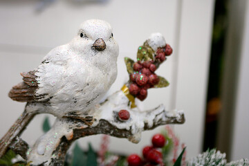 Figurine of white Christmas bird sitting on a branch with red berries