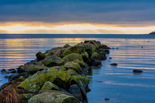 A beautiful sunset over the green boulders on a wave breaker. Photo from Hallevik, Blekinge county, Sweden