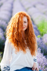 Summer portrait of a beautiful girl with long curly red hair. European girl in lavender field. Wavy Red Hair
