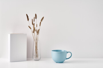 A transparent vase with dry branches, bottle of water with a cork stopper and a book on a white background. Minimalism, eco-materials in the interior decor. Copy space, mock up