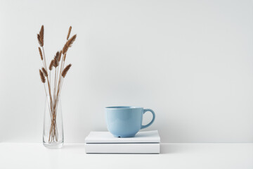 A mug on a stack of books and a transparent vase with dried flowers. Eco-friendly materials in interior decor, minimalism. Copy space, mock up.