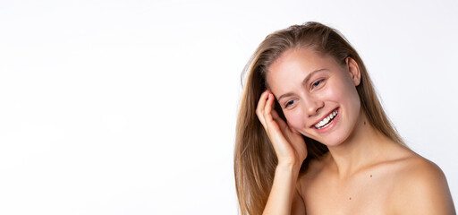 Fototapeta premium Smiling blonde on a white background straightens her long hair. Empty space. Skinimalism and natural skin texture