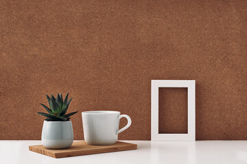 Frame, houseplant in a pot and a white cup, cork background. Mock up, copy space. Folk.