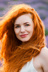 Summer portrait of a beautiful girl with long curly red hair. European girl in lavender field. Wavy Red Hair