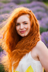 Summer portrait of a beautiful girl with long curly red hair. European girl in lavender field. Wavy Red Hair