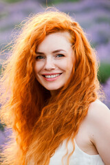 Summer portrait of a beautiful girl with long curly red hair. European girl in lavender field. Wavy Red Hair