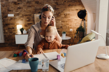 Mid adult working mother taking notes during conference call at home.