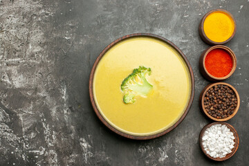 Creamy broccoli soup in a brown bowl and different spices on the left side of gray background