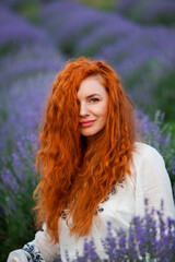 Summer portrait of a beautiful girl with long curly red hair. European girl in lavender field. Wavy Red Hair