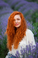 Summer portrait of a beautiful girl with long curly red hair. European girl in lavender field. Wavy Red Hair
