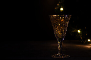 Glass with white wine with garland lights on the background. dark picture. Golden beverage in the glass. Beautiful lights reflected in the glass.