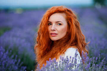 Summer portrait of a beautiful girl with long curly red hair. European girl in lavender field. Wavy Red Hair