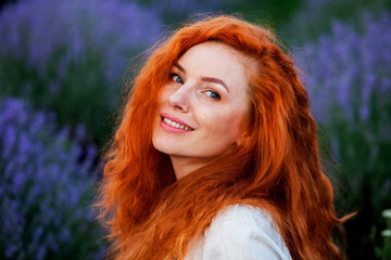 Summer portrait of a beautiful girl with long curly red hair. European girl in lavender field. Wavy Red Hair