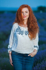 Summer portrait of a beautiful girl with long curly red hair. European girl in lavender field. Wavy Red Hair