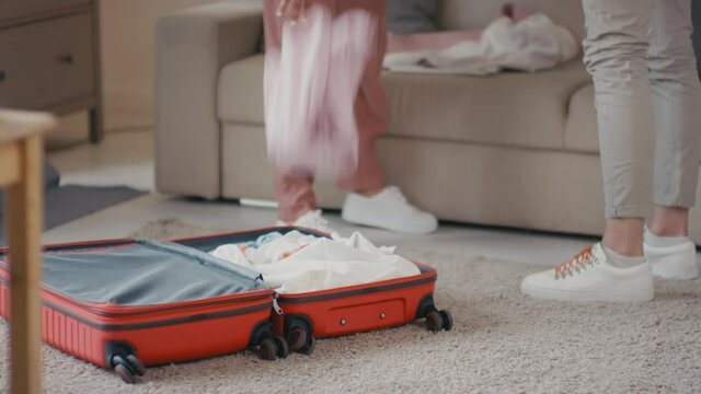 Low-section footage of unhappy married couple separating after serious conflict and woman roughly throwing clothes in suitcase getting ready to leave and divorce