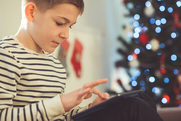 Teenager boy playing or studing with laptop near christmas tree iat home