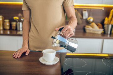 Fototapeta na wymiar Close up of a man in beige tshirt pouring coffee to the cup