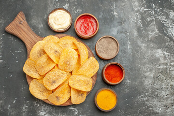 Homemade chips spices and mayonnaise with ketchup on wooden cutting board on gray background